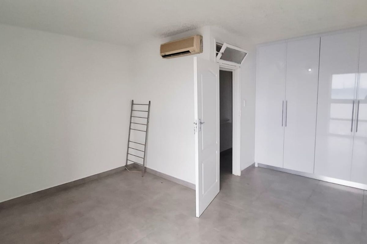 A bright bedroom featuring modern white built-in cupboards, tiled flooring, and a wall-mounted air conditioning unit.