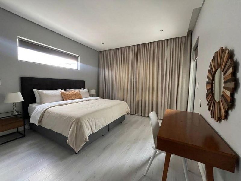 A well-maintained bedroom featuring modern laminate flooring, recessed downlighting, and large windows with full-height curtains for privacy.