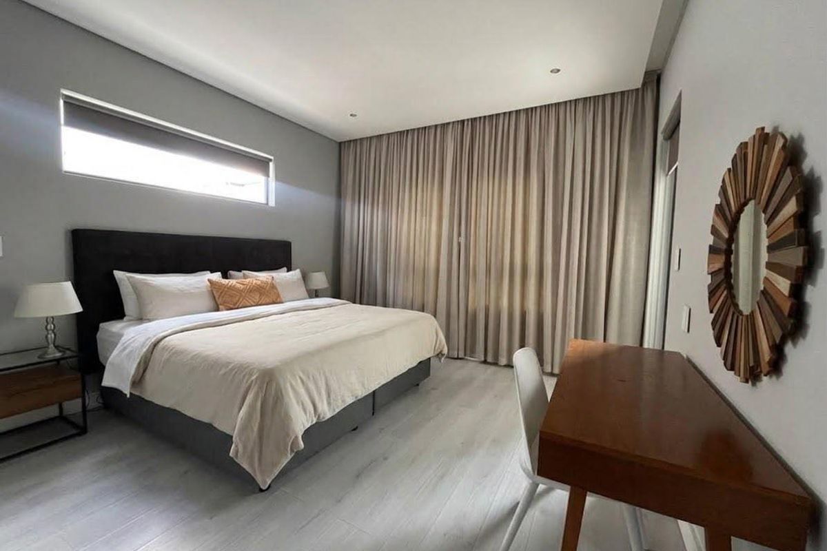 A well-maintained bedroom featuring modern laminate flooring, recessed downlighting, and large windows with full-height curtains for privacy.