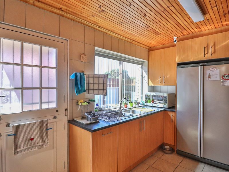 A functional kitchen featuring laminate cabinetry, a stainless steel sink, tiled backsplash, and a distinctive wooden ceiling with tiled flooring.