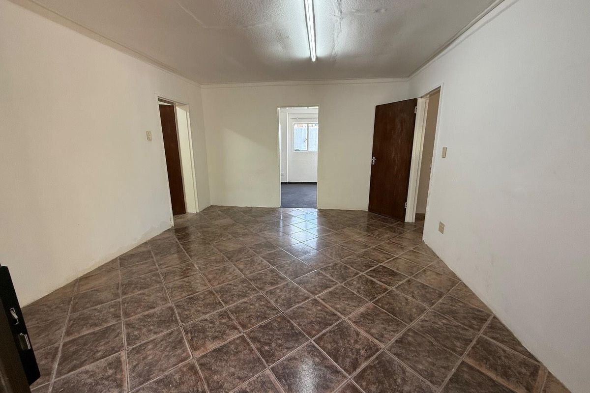 An empty living area featuring dark ceramic floor tiles, white walls, and multiple interior doorways leading to adjacent rooms.