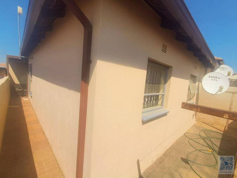 Rear exterior view of the property featuring a paved walkway, security bars on windows, and satellite dish installations.