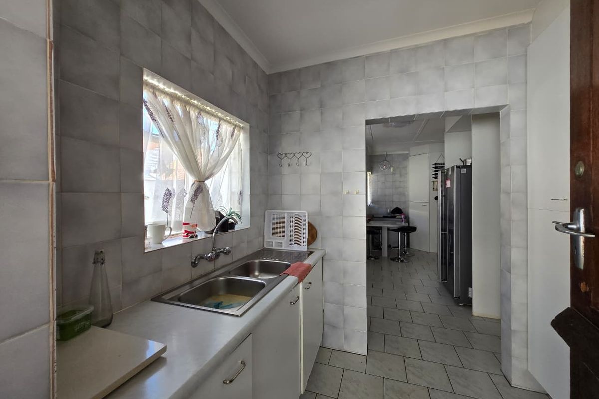 A functional kitchen area featuring a double stainless steel sink, tiled walls, and tiled flooring, with an open transition to an adjacent dining space.