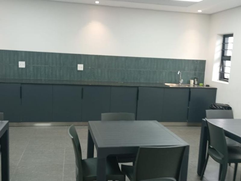 A clean, modern industrial kitchen area featuring dark cabinetry, a tiled backsplash, integrated sink, and recessed lighting in a drop ceiling.