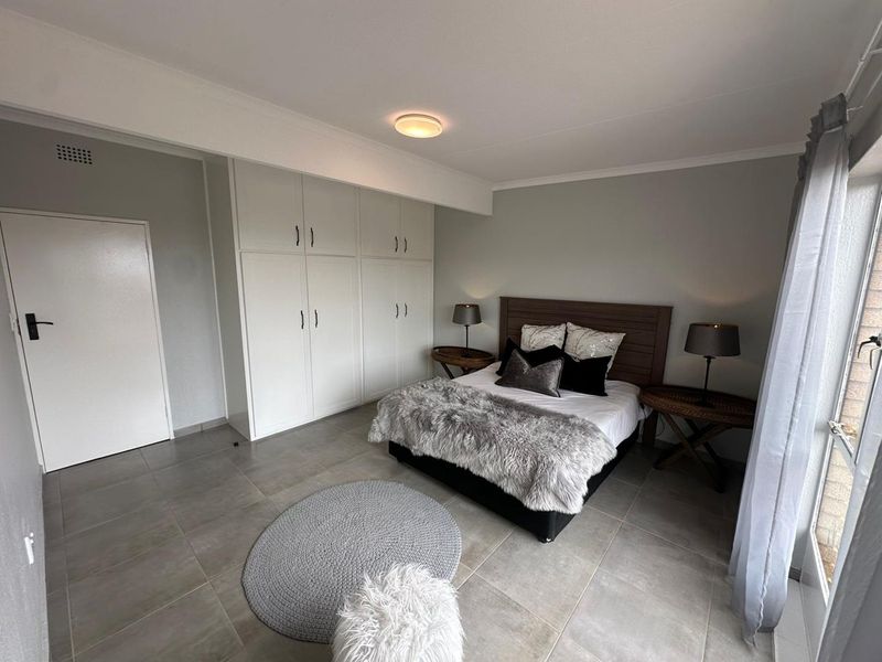 A well-maintained bedroom featuring neutral tiled flooring, ample built-in cupboard storage, and direct access to an outdoor area via a sliding door.