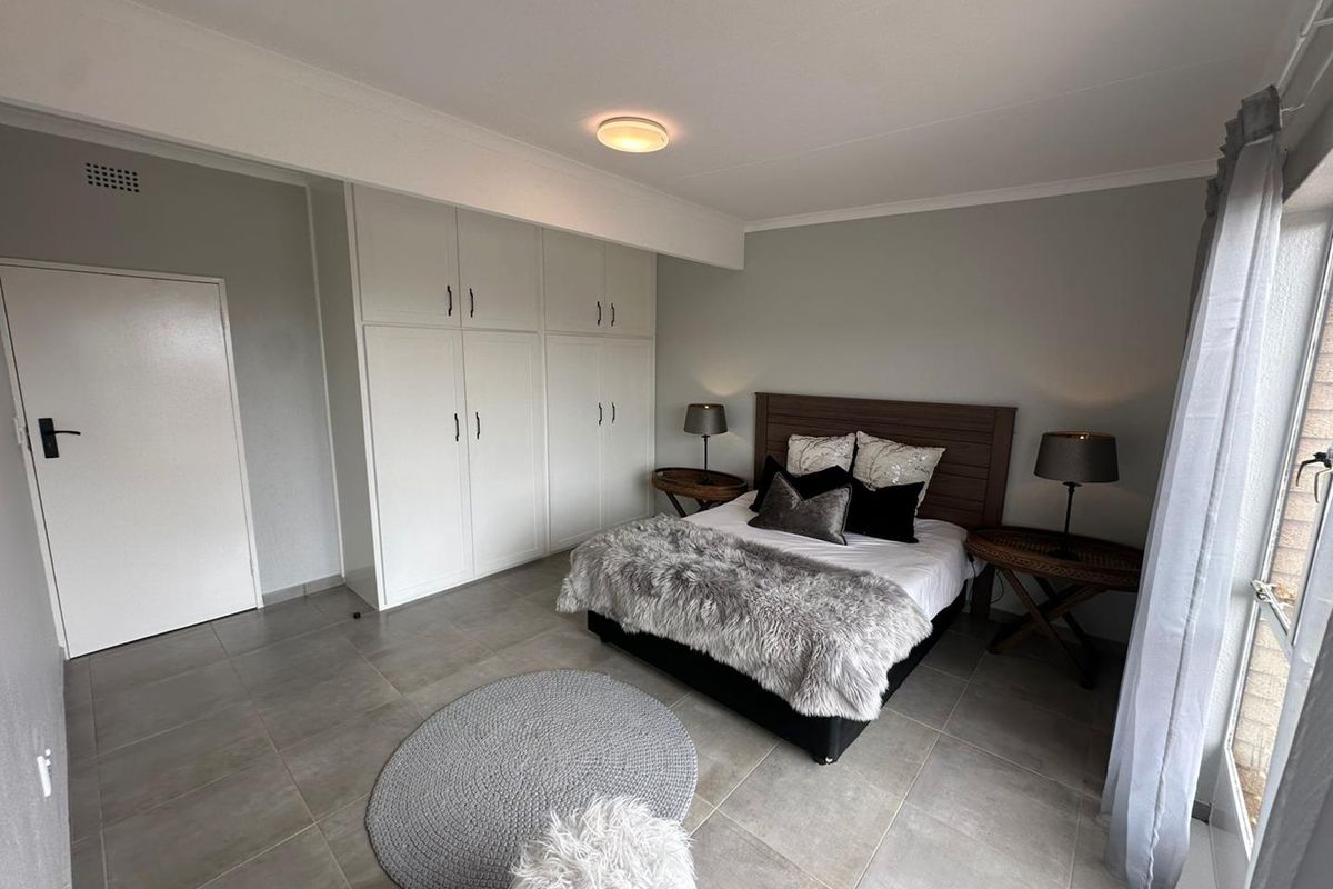 A well-maintained bedroom featuring neutral tiled flooring, ample built-in cupboard storage, and direct access to an outdoor area via a sliding door.