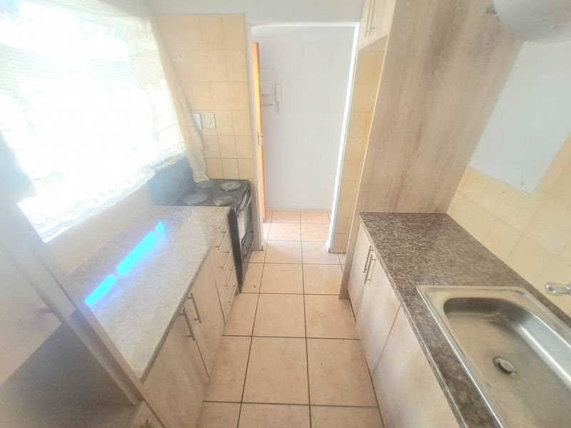 A functional galley-style kitchen featuring granite countertops, built-in cabinetry, a stainless steel sink, and an electric stove with tiled flooring and backsplash.