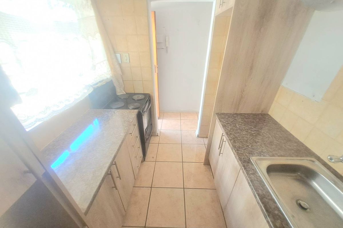 A functional galley-style kitchen featuring granite countertops, built-in cabinetry, a stainless steel sink, and an electric stove with tiled flooring and backsplash.