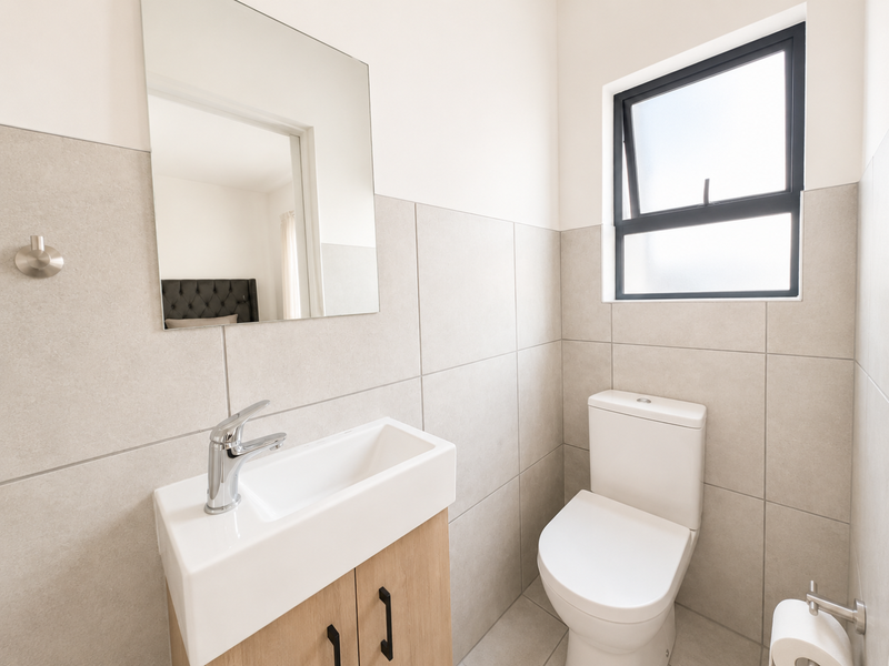 Modern guest bathroom featuring neutral wall tiles, a sleek vanity with basin, and a contemporary toilet.