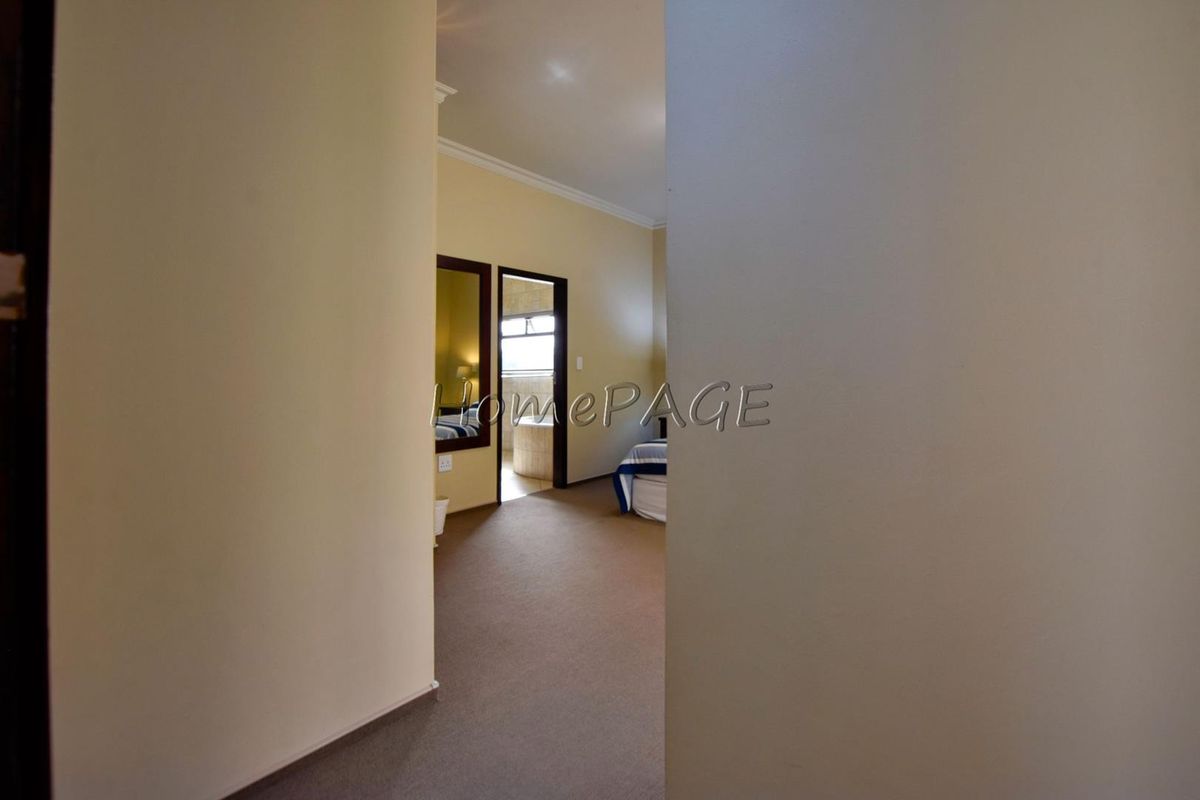 A view from a hallway into a bedroom featuring carpeted flooring and coved ceilings, with an adjacent bathroom visible through the doorway.