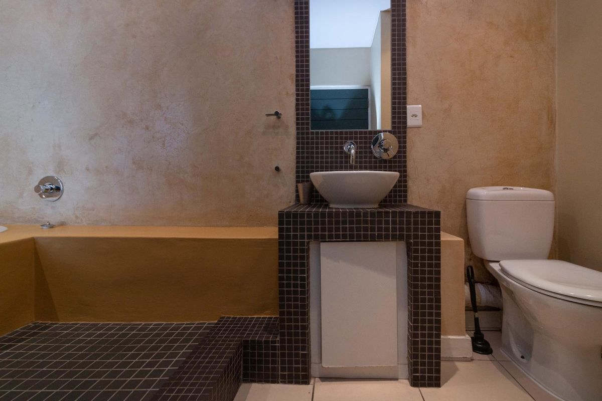 A bathroom featuring a built-in bathtub, a tiled vanity with a vessel sink, and a standard toilet with mosaic tile accents.