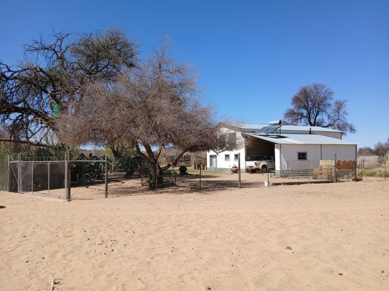 Exterior view of a small holding property featuring a metal-roofed structure with a solar water heater and surrounding wire fencing.