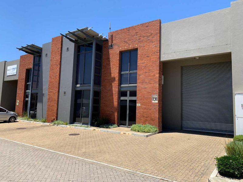 Modern industrial unit featuring a brick facade, large aluminium windows, and a secure roller shutter door with a paved driveway approach.