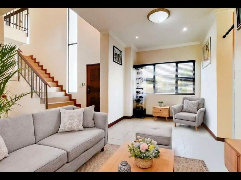 A bright living room featuring tiled floors, a staircase with a wrought iron balustrade, and a large vertical window providing natural light.