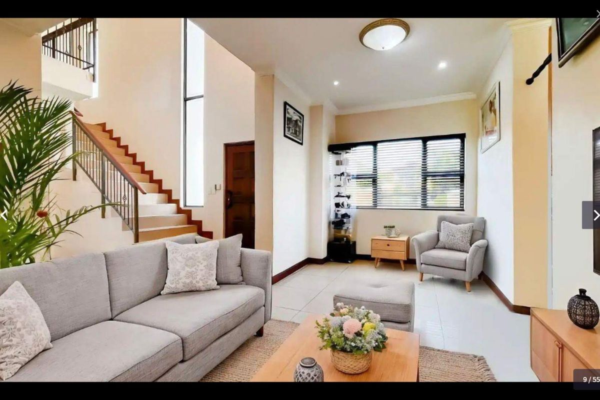 A bright living room featuring tiled floors, a staircase with a wrought iron balustrade, and a large vertical window providing natural light.