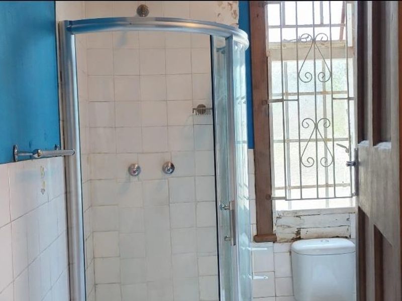 A functional bathroom featuring a corner shower enclosure, toilet, and tiled walls, requiring cosmetic updates to the paint and window frame.