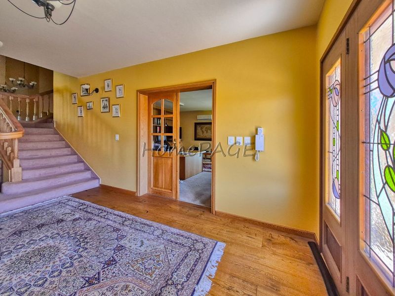 Welcoming entrance hall featuring hardwood flooring, a carpeted staircase with wooden railing, and a decorative stained glass front door.