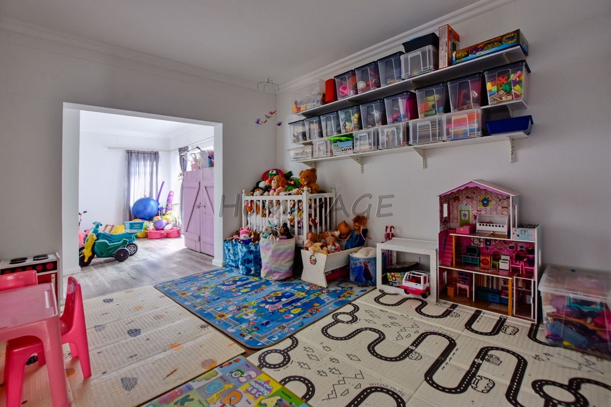A spacious bedroom currently utilized as a playroom, featuring wall-mounted storage shelving and durable laminate flooring with access to an adjoining room.