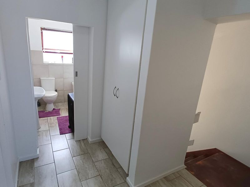 A bright hallway featuring tiled flooring, a built-in storage cupboard, and access to an adjacent bathroom and staircase.