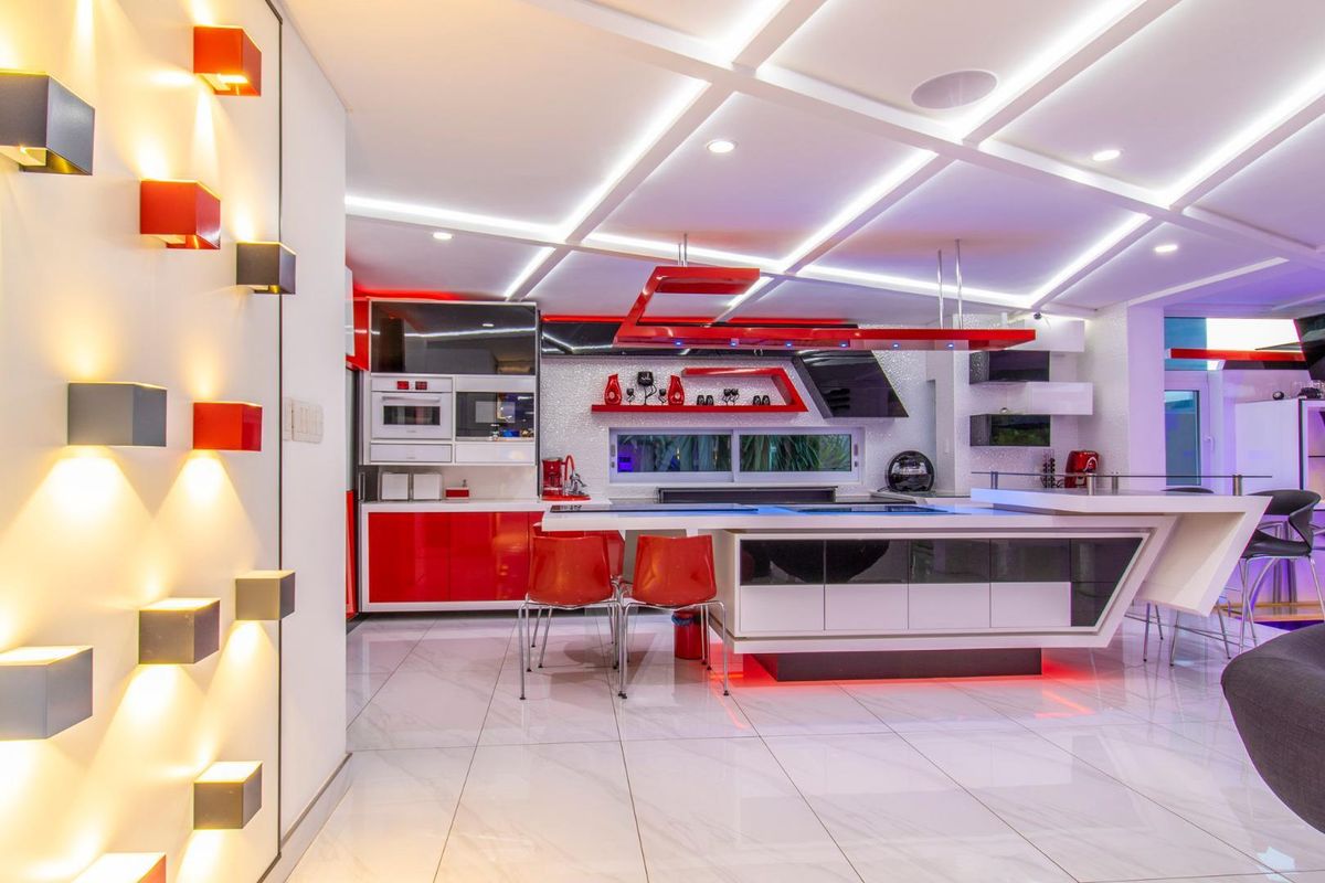 Modern, high-gloss kitchen featuring a large central island, integrated appliances, custom red and white cabinetry, and sophisticated recessed ceiling lighting.