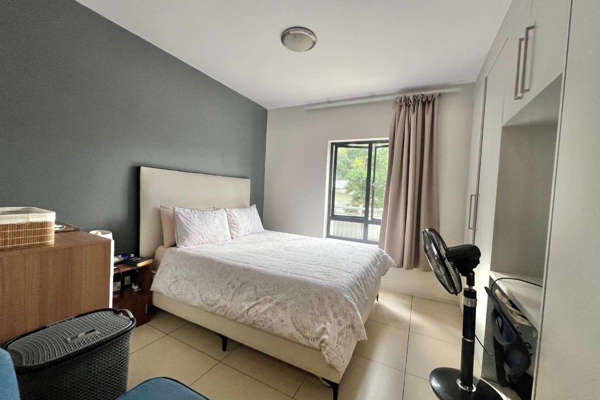 A well-lit bedroom featuring neutral tiled flooring, a built-in wardrobe, and a large window providing natural light.