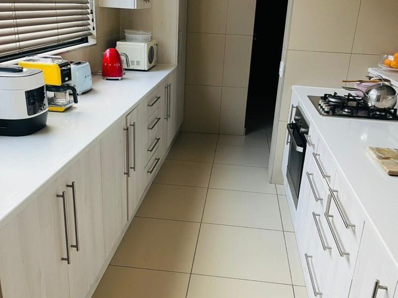 Modern galley-style kitchen featuring light wood-grain cabinetry, white stone countertops, integrated gas hob, built-in oven, and neutral floor-to-ceiling wall tiles.