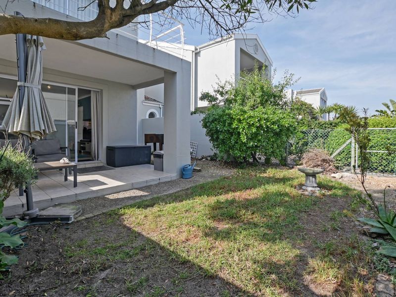 A rear townhouse view featuring a covered patio with tiled flooring, sliding glass doors, and a private garden area with lawn and perimeter fencing.