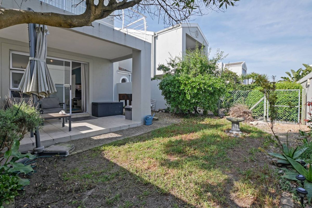 A rear townhouse view featuring a covered patio with tiled flooring, sliding glass doors, and a private garden area with lawn and perimeter fencing.