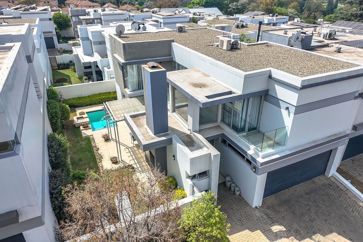 Aerial view of a modern cluster home featuring a flat roof design, private swimming pool, paved driveway, and integrated garage within a secure estate.