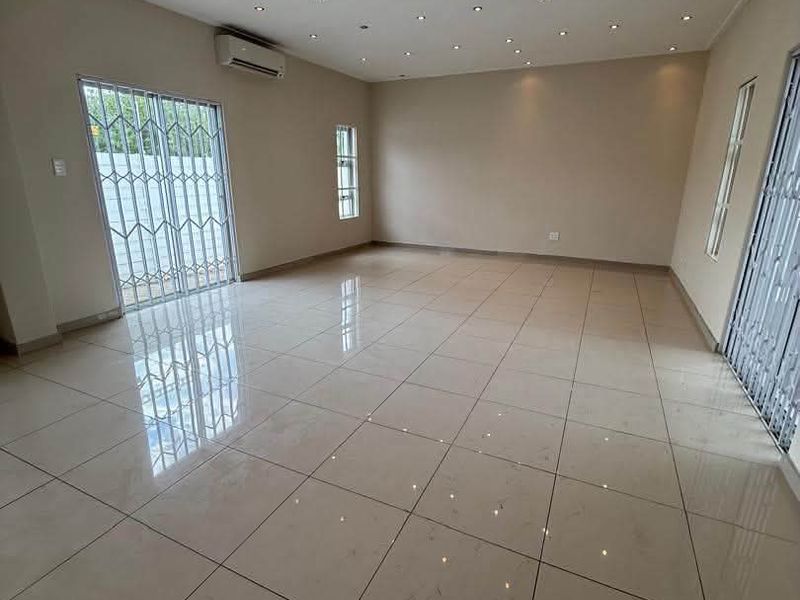 Spacious, empty living area featuring polished floor tiles, recessed downlighting, a split-system air conditioner, and secure sliding glass doors leading outdoors.