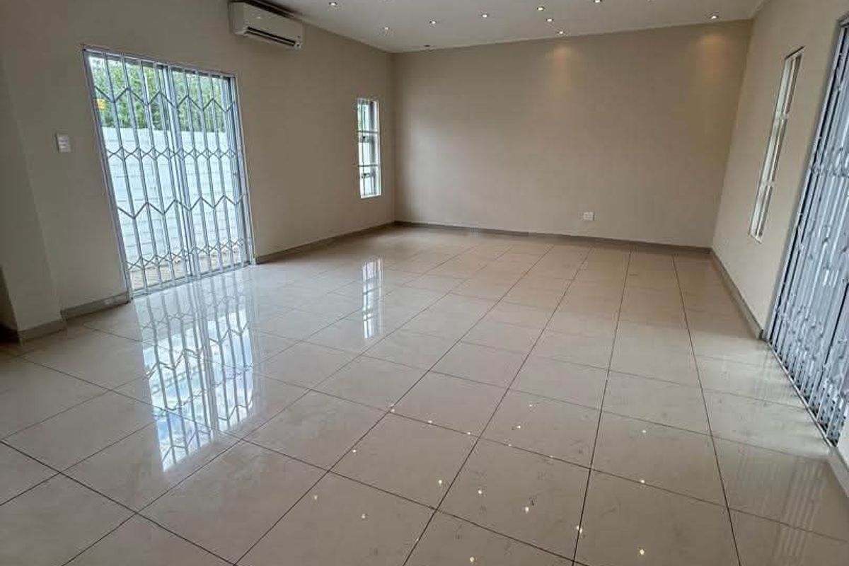 Spacious, empty living area featuring polished floor tiles, recessed downlighting, a split-system air conditioner, and secure sliding glass doors leading outdoors.