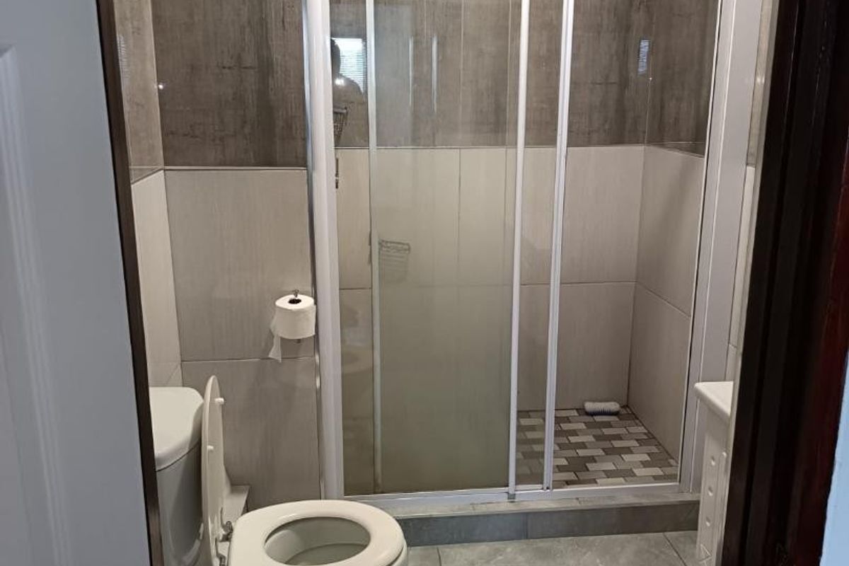 A clean, modern bathroom featuring a glass sliding shower enclosure, neutral wall and floor tiling, and a standard toilet.