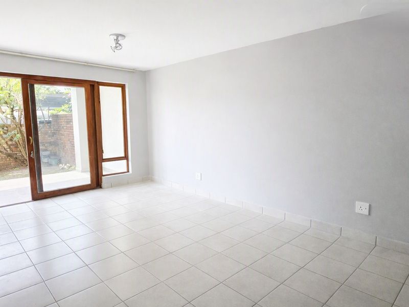 An empty, bright living room featuring neutral tiled flooring and a large sliding glass door providing access to the outdoor area.