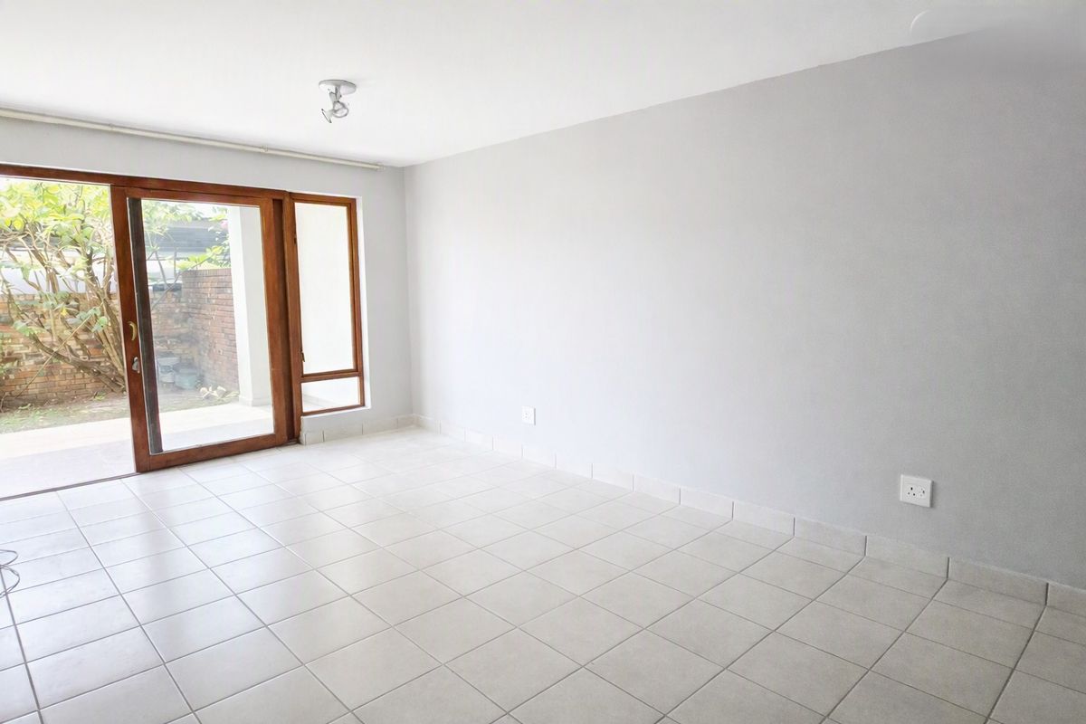 An empty, bright living room featuring neutral tiled flooring and a large sliding glass door providing access to the outdoor area.