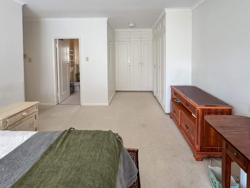 Spacious bedroom featuring extensive built-in cupboards, neutral carpeting, and direct access to an en-suite bathroom.