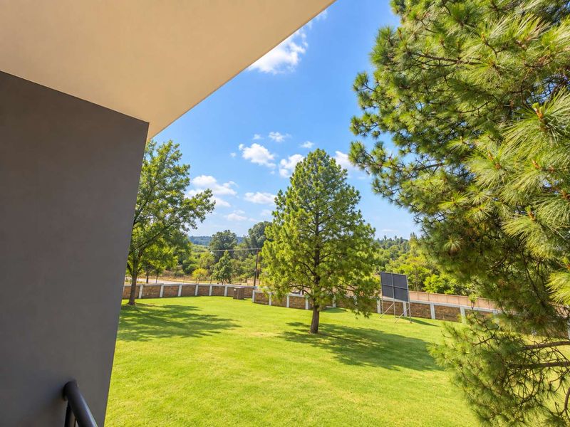 A view from a covered balcony overlooking a well-maintained green lawn and surrounding trees.
