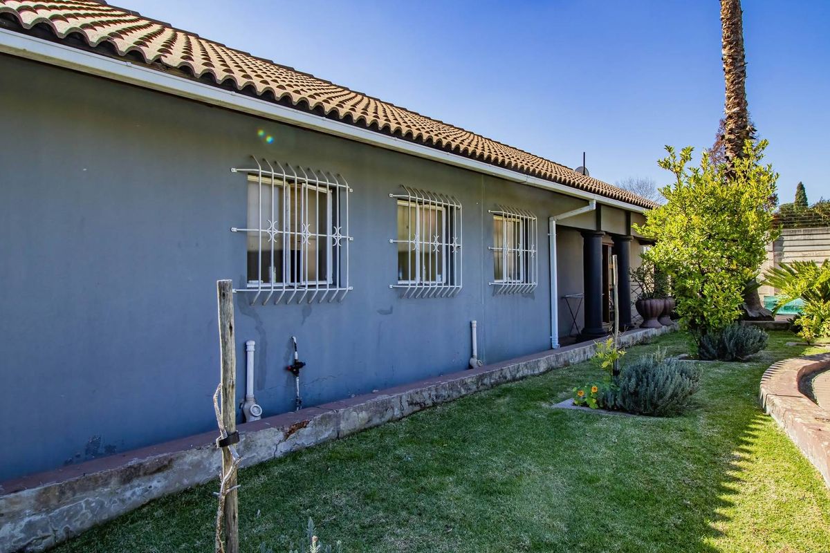 Rear view of the house featuring a tiled roof, grey exterior walls, and security bars on windows, overlooking a landscaped garden area.
