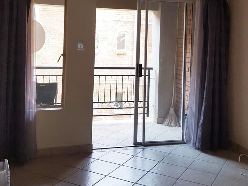 A bright, empty living area featuring tiled flooring and a sliding glass door that opens onto a private balcony.