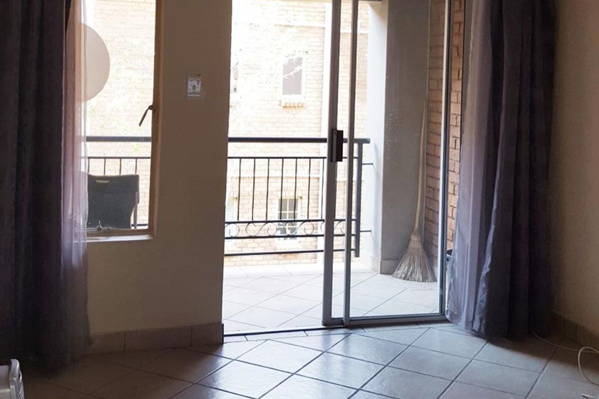 A bright, empty living area featuring tiled flooring and a sliding glass door that opens onto a private balcony.