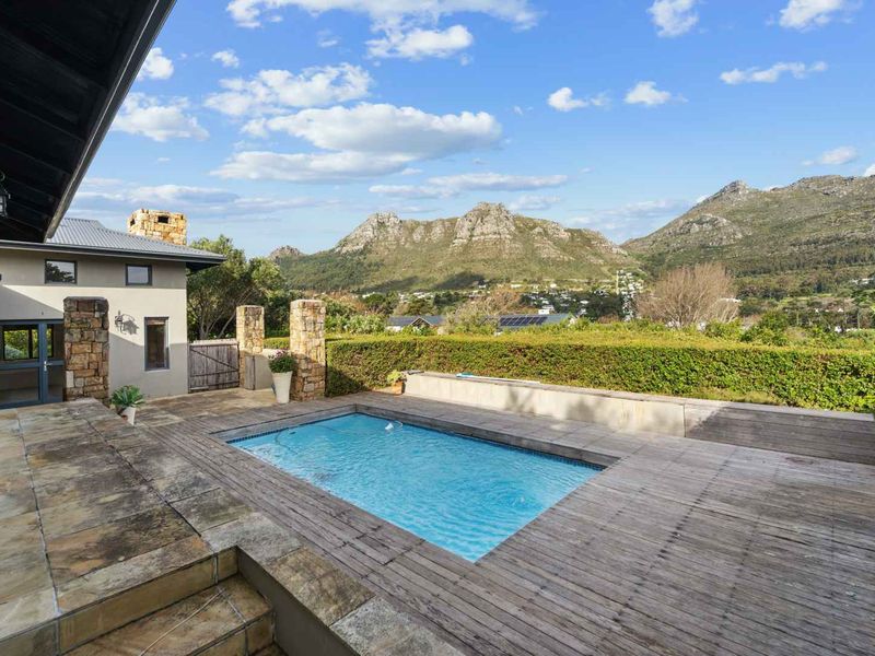Outdoor pool area featuring timber decking, stone paving, and a retaining wall, set against a scenic mountain backdrop.