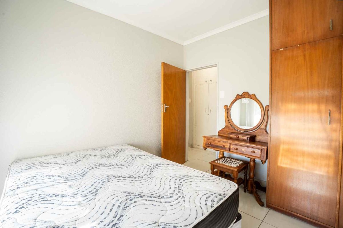 A bedroom featuring tiled flooring, a built-in wooden wardrobe, and coved ceiling details, with an adjacent hallway visible through the doorway.
