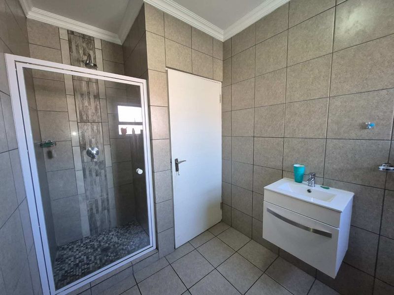 A modern bathroom featuring a walk-in shower with glass enclosure, wall-mounted vanity, and neutral ceramic tiling throughout.