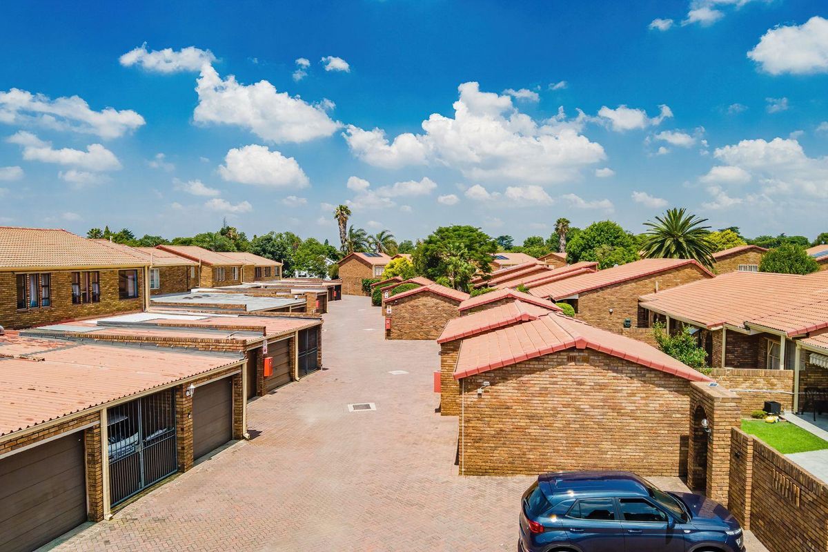 Aerial view of a townhouse complex featuring brick facades, tiled roofs, and paved driveway access to individual garage units.