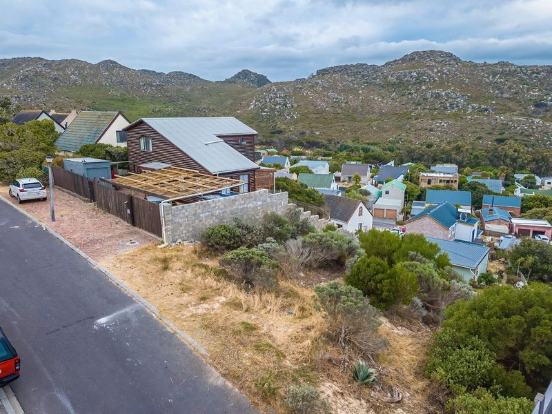 Aerial view of a residential property featuring a timber-clad home with a metal roof, unfinished pergola, and concrete boundary wall in a mountainous setting.