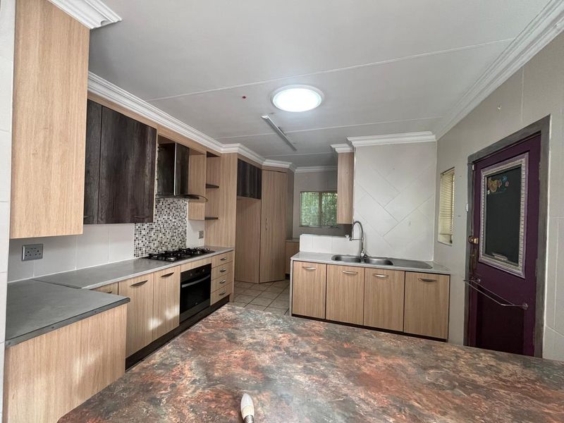 A functional kitchen featuring light wood cabinetry, built-in oven and hob, double sink, and a central island with a stone-look countertop.