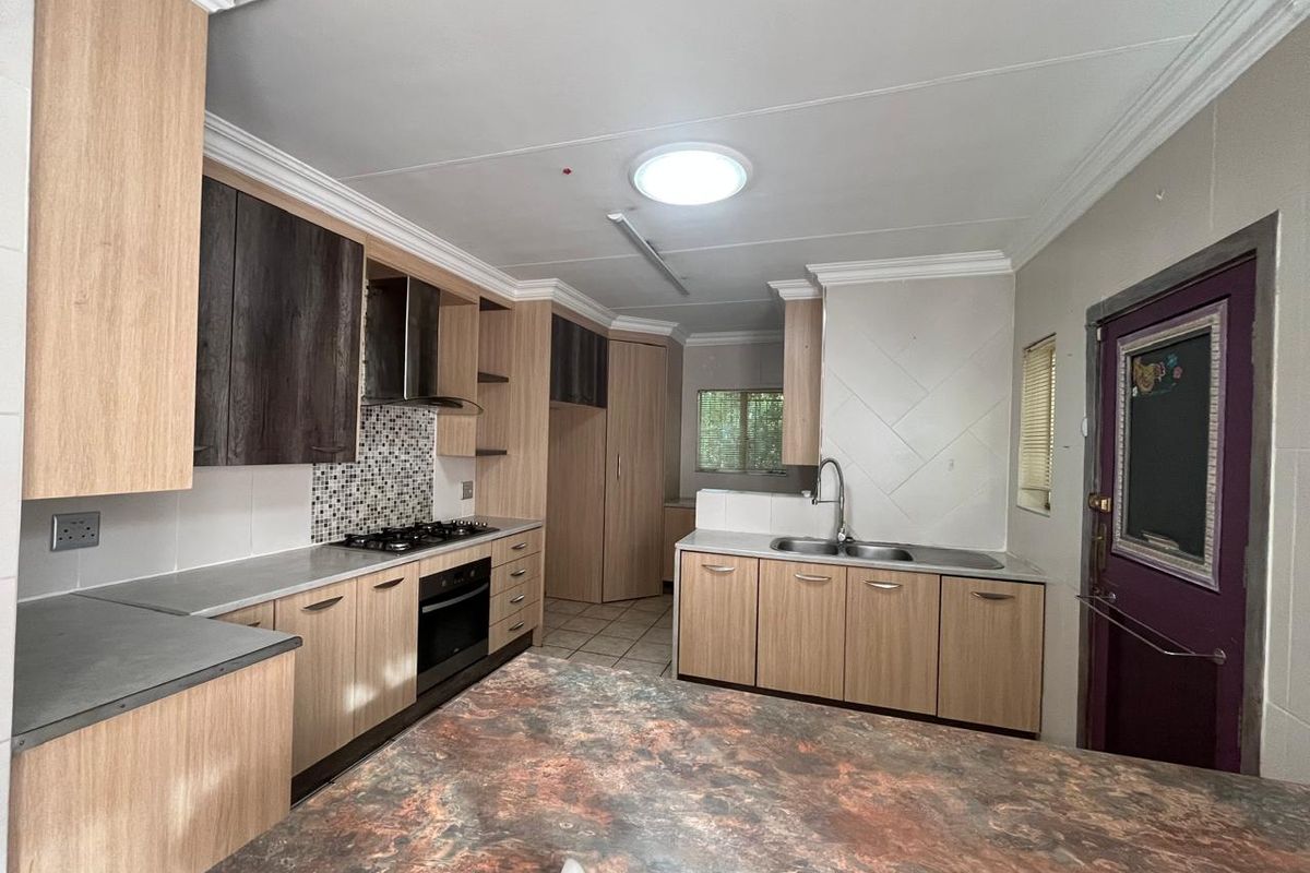 A functional kitchen featuring light wood cabinetry, built-in oven and hob, double sink, and a central island with a stone-look countertop.