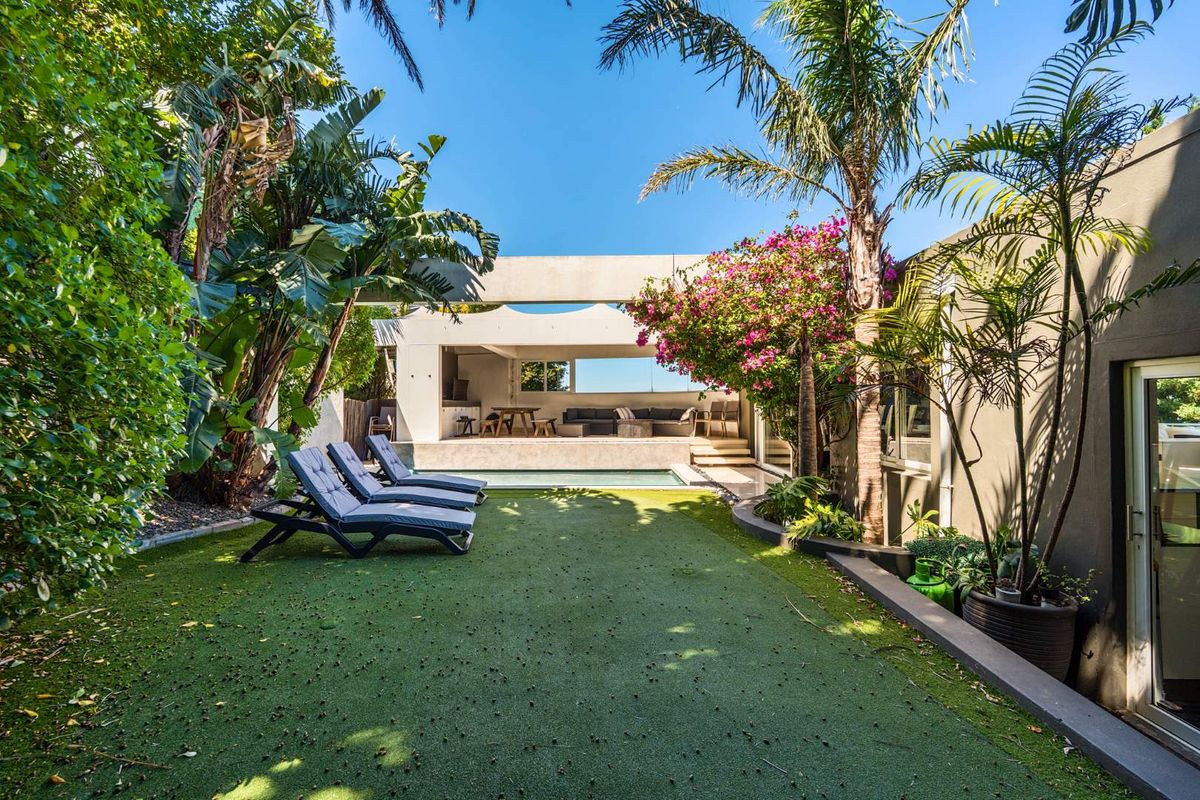 A well-maintained rear garden featuring an artificial lawn, a swimming pool, and a covered patio area with integrated architectural concrete elements.