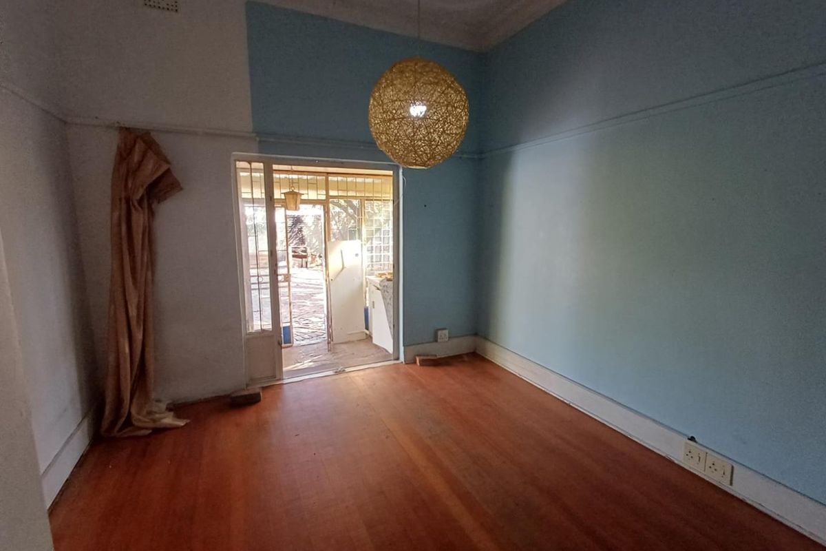 An empty living room featuring original hardwood flooring, ornate ceiling cornices, and direct access to an outdoor patio area through a security gate.