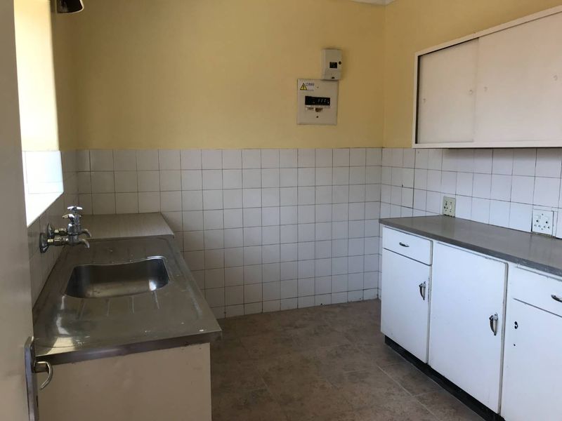 A functional, empty kitchen space featuring a stainless steel sink, tiled splashback, and built-in cabinetry with laminate countertops.