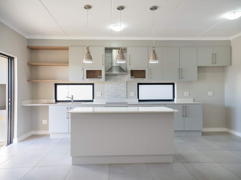 Modern kitchen featuring light grey cabinetry, a central island, stone countertops, open shelving, and integrated extractor fan, finished with neutral floor tiles.